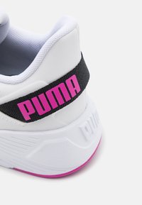 Biała tenisówka z czarnym materiałowym paskiem z różowym logo "PUMA". Teksturowana podeszwa z różowym akcentem na spodzie.