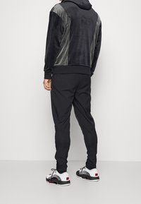 Schwarzer Velours-Hoodie mit grauen Schulterakzenten, kombiniert mit schwarzen elastischen Hosen und mustergemäßen Sportschuhen mit weißen, roten und schwarzen Details.
