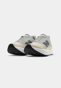 Une paire de chaussures de course New Balance gris clair avec des semelles médianes blanches épaisses et des semelles extérieures noires texturées, vue de biais sur fond blanc.