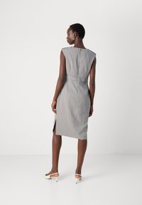 Robe à carreaux noir et blanc avec une silhouette ajustée, des manches courtes et des fentes sur les côtés. Stylée avec des chaussures à talons bas de couleur claire.