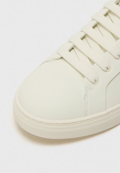 White synthetic leather sneaker with flat laces, rounded toe, smooth texture, and a textured rubber sole. Minimalist design focus.