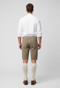 Men's knee-length shorts in beige fabric, paired with a white long-sleeve shirt. Features back pocket and textured ivory knee-high socks.