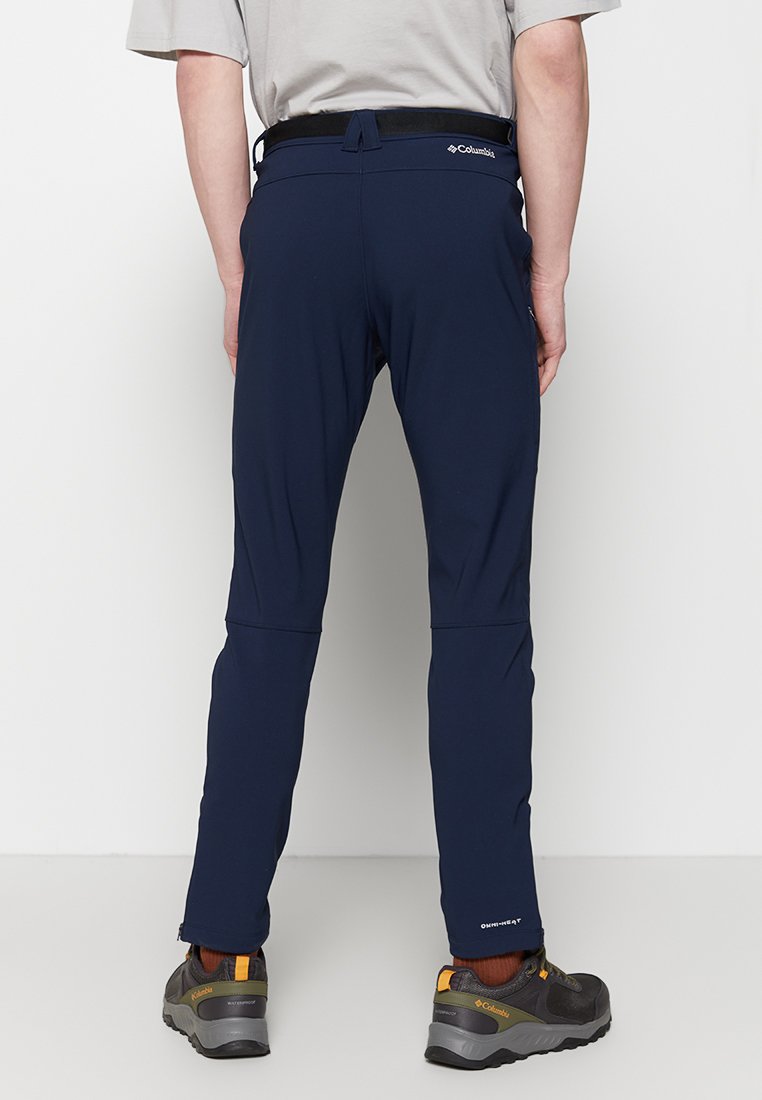Pantalones exteriores en color navy con un tejido texturizado, cinturilla elástica y bolsillos con cremallera. Combinados con zapatos de senderismo grises y negros.