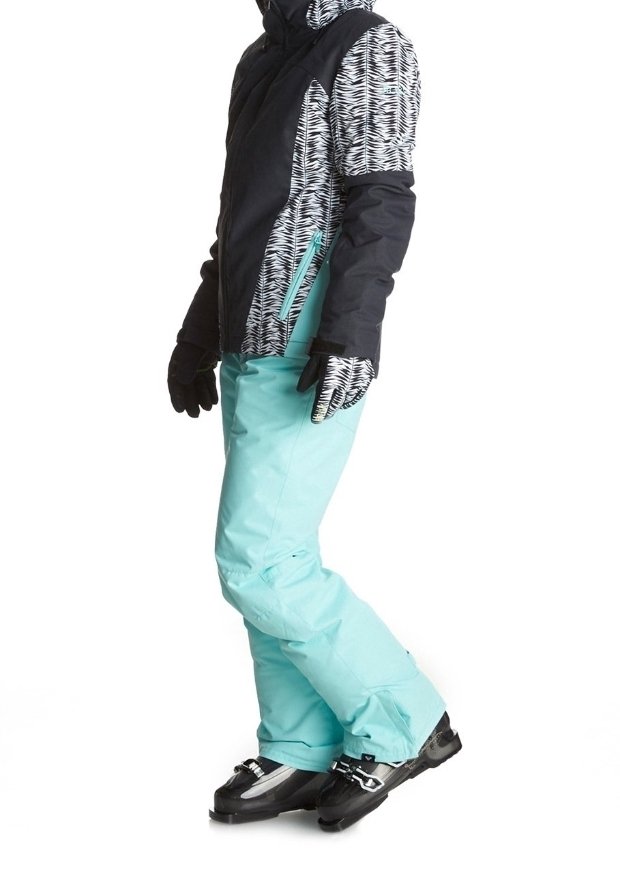 Skiausrüstung mit einer gemusterten schwarz-weißen Jacke, mintgrünen Hosen, schwarzen Handschuhen und Skischuhen mit silbernen Akzenten.