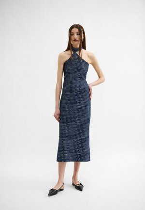 Abito halter neck navy con corpetto aderente, orlo all'altezza del ginocchio e piccoli motivi bianchi sparsi. Abb paired con scarpe nere flat.