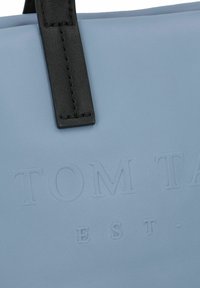Sac en cuir bleu clair avec une surface texturée et une poignée en cuir noir. Présente un texte en relief "TOM TAIL" et "EST-".