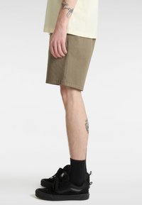 Khaki bavlněné šortky s volným střihem, s čistým lemem a bočními kapsami, doplněné černými teniskami a ponožkami do půli lýtek.