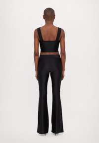 Top nero corto con spalline larghe e design senza cuciture, abbinato a pantaloni neri a vita alta e svasati. Tessuto liscio ed elastico in tutto.