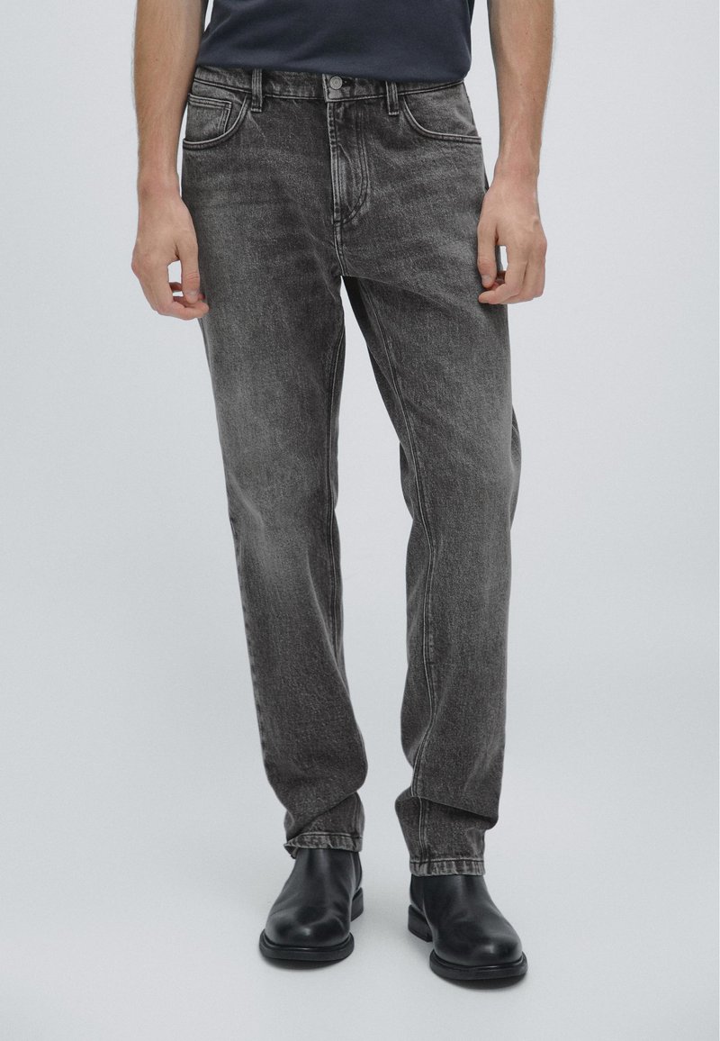 Svarta jeans av denim med en lätt blekt finish, femfickorsdesign och rak benpassform, tillsammans med svarta ankelstövlar.