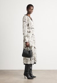 White dress with black sketches, long sleeves, belted waist, tiered hem. Black woven handbag and knee-high black boots.