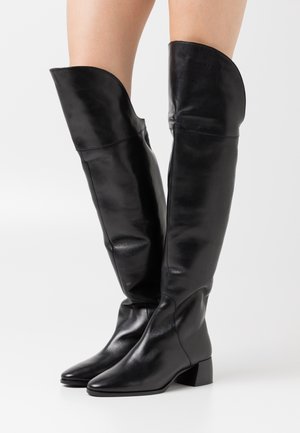 Botas altas de cuero negro con un diseño elegante, punta afilada y un tacón bajo tipo bloque. Presentan un borde superior curvado y una textura suave.