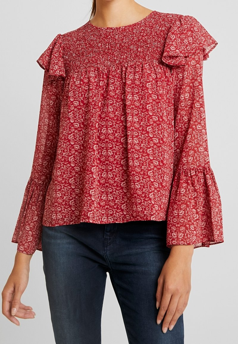 Rød blomsterbluse med smocked halsudskæring, volangærmer og flared ærmer. Letvægtsstof med et delikat blomster mønster.