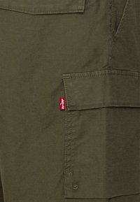 Shorts cargo vert olive avec poche rabat à l'avant, étiquette rouge contrastante Levi's, tissu durable et détails de coutures visibles.