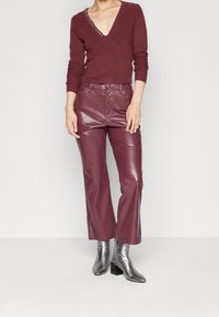 Bordowy sweter dzianinowy z dekoltem w serek i teksturowanymi detalami, zestawiony z wysokim stanem bordowych skórzanych spodni i metalicznymi botkami na kostkę.