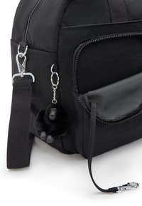 Black fabric backpack with a zippered pocket, featuring a furry gorilla keychain and a webbed shoulder strap. Silvery hardware accents.