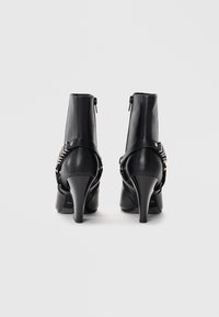 Bottines en cuir noir avec un talon haut, dotées d'une fermeture éclair et d'un détail de bande métallique sur le côté. Texture lisse.