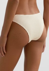 Kremno teksturiran spodnji del bikinija z vtisnjenim tkanim vzorcem. Visok pas s gladkim pasom in minimalno pokritostjo na zadnji strani.