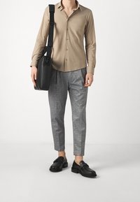 Beige långärmad knappad skjorta, grå mönstrade byxor, svarta läderskor och en svart budväska.