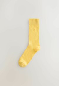 Calcetín de algodón amarillo con puño acanalado, textura suave y puntera reforzada. Presenta un pequeño logo encima del tobillo.