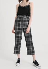 Top de tirantes negro con detalles de encaje, combinado con pantalones de pierna ancha de cuadros en blanco y negro de talle alto, que cuentan con un cinturón y detalles de botones.