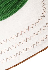 Tissu vert rond avec une surface texturée cousue sur un matériau blanc, présentant des coutures en zigzag marron et un bord texturé marron.