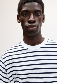 Gestreiftes T-Shirt mit navyblauen und weißen horizontalen Streifen, aus weichem Stoff gefertigt, mit rundem Ausschnitt und kurzen Ärmeln. Einfaches Design.