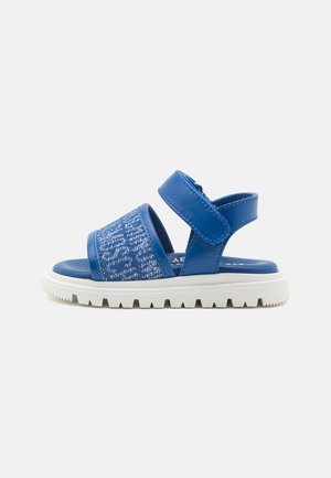 Sandali blu con una tomaia in tessuto testurizzato, doppi cinturini in velcro e una suola in gomma bianca con un battistrada decorato.