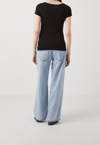 Svart kortärmad topp tillsammans med ljusblå vida jeans. Toppen är figursydd; jeansen har en avslappnad silhuett med bakfickor.