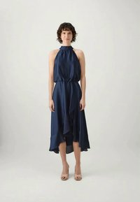 Sötétkék, nyakba akasztható ruha, testhez simuló felsőrésszel, elasztikus derékkal és aszimmetrikus fodros aljjal. Simogató, folyékony anyag, diszkrét fényű.