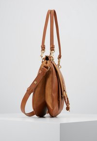 Brun læderhåndtaske med en kontrastfarvet ruskindsstruktur, dobbelt skulderremme, guldhardwaredetaljer og et rummeligt opdelt interiør.