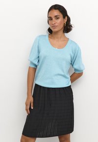 Light blue knit top with short puff sleeves and a rounded neckline paired with a black, knee-length textured skirt featuring a checkered pattern.
