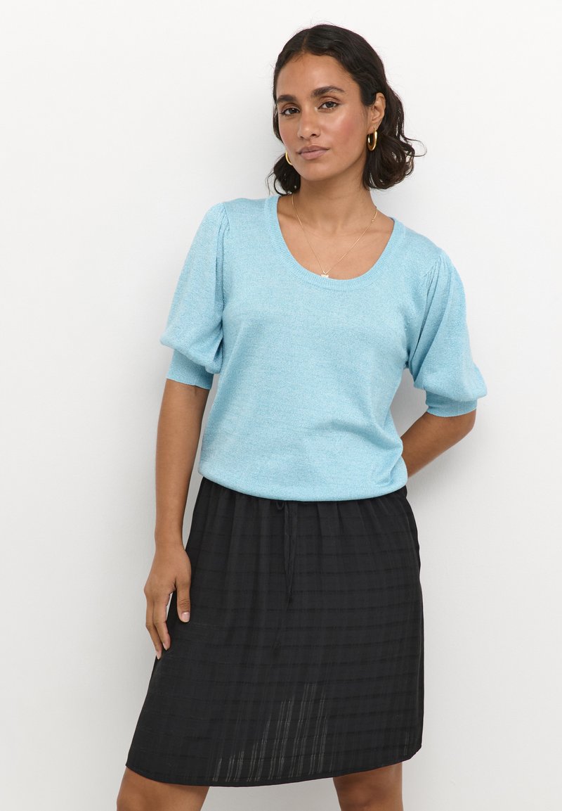 Light blue knit top with short puff sleeves and a rounded neckline paired with a black, knee-length textured skirt featuring a checkered pattern.