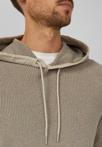 Beige strukturierter Hoodie mit einer Kapuze mit Kordelzug, geripptem Stoff und einem glatten Innenfutter. Akzente durch dünne, metallisch bestrichene Kordeln.