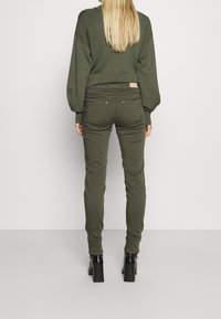 Olivgrön tight passande byxor med en slät textur, femficksdesign och en liten logotyp på baksidan av midjebandet.