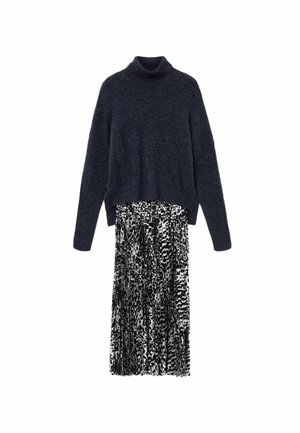 Pull à col roulé bleu marine avec texture côtelée, associé à une jupe plissée à motif noir et blanc. Manches longues et coupe décontractée.