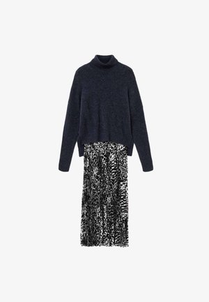 Pull à col roulé bleu marine avec texture côtelée, associé à une jupe plissée à motif noir et blanc. Manches longues et coupe décontractée.