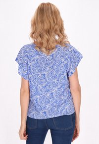 Blusa blu con motivo paisley, maniche a sbuffo, in tessuto leggero e vestibilità comoda, abbinata a jeans fitted blu scuro.