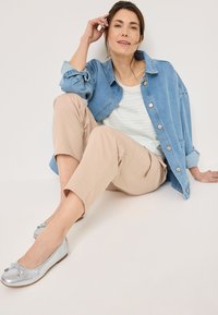 Camicia di denim, azzurra chiara con bottoni, sopra una maglietta a righe bianche e azzurre. Pantaloni beige a tre quarti e ballerine argentate lucide con fiocchi.