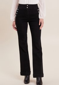 Pantalons noirs taille haute avec une coupe droite. Présente trois boutons métalliques à l'avant et des accents de boutons décoratifs sur les hanches.