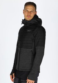 Giacca nera isolata con parte superiore trapuntata, maniche testurizzate, tasche con zip e cappuccio. Progettata per uso all'aperto.