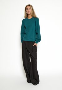 Felpa teal con collo a girocollo a coste e pantaloni neri a gamba larga. Entrambi i capi presentano una vestibilità comoda e una texture di tessuto liscia.