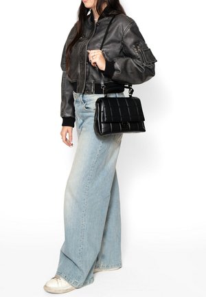 Borsa a tracolla nera trapuntata con forma strutturata, manico corto e chiusura magnetica, abbinata a una giacca di pelle cropped e jeans a gamba larga.