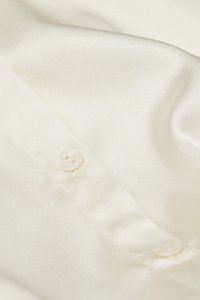 Cream satin fabric with a smooth texture, featuring two buttons in a pale color, partially unbuttoned, showcasing a soft drape.