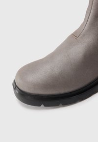 Primer plano de la punta de una bota de ante gris con suela de goma negra en un fondo blanco.