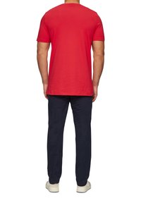 Rode katoenen T-shirt met korte mouwen en een ronde halslijn, gecombineerd met donkerblauwe broek en lichtgekleurde schoenen, gezien vanuit de achterkant.