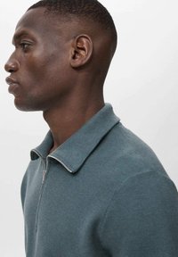 Men's zip-up collar sweater in a muted teal color. Ribbed texture and a silver zipper accent on the front. Short sleeves and fitted design.