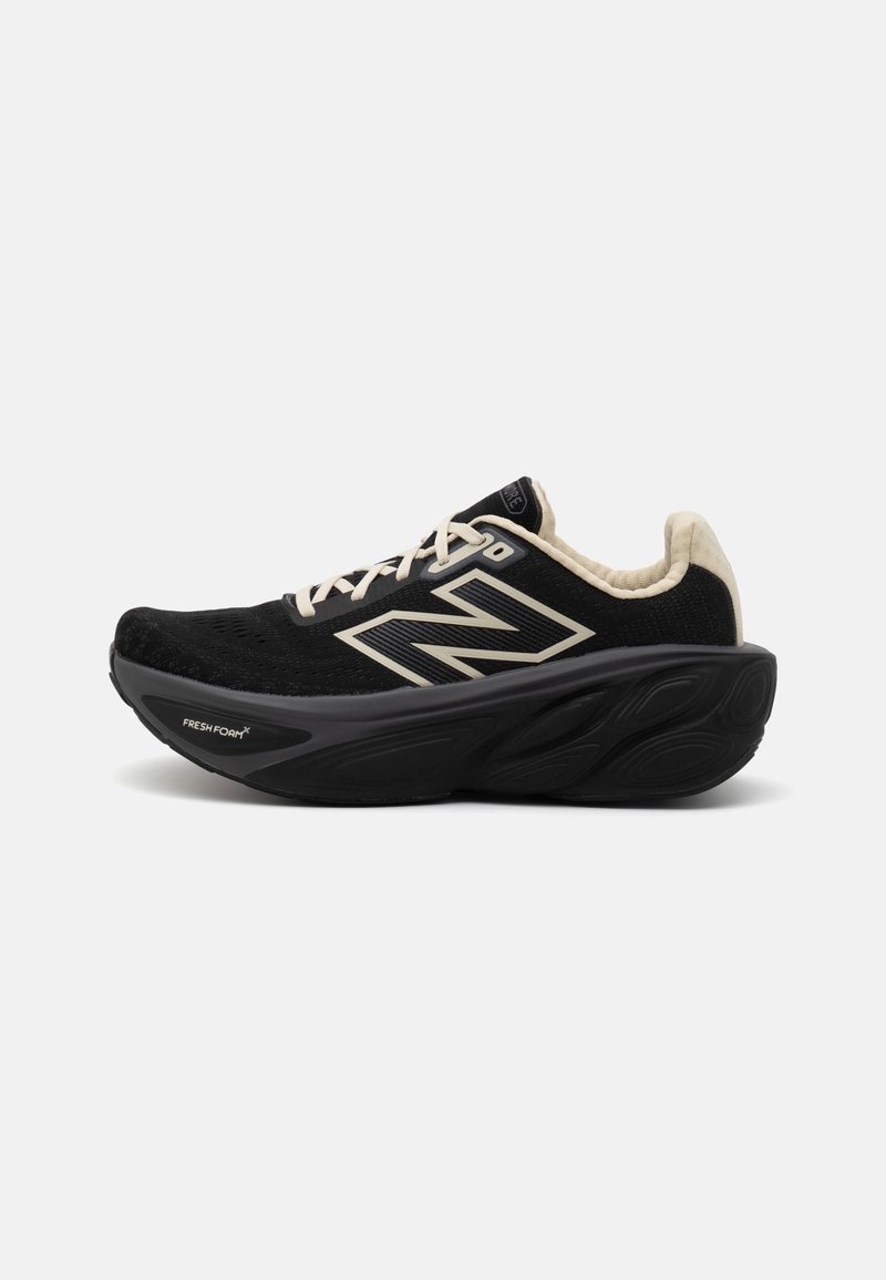 Chaussure de sport noire avec des lacets et une doublure beige, dotée d'une semelle épaisse et rembourrée et d'un grand logo New Balance sur le côté.