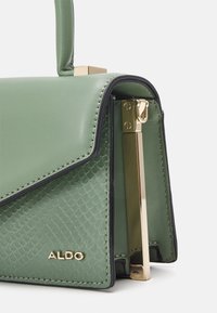 Grön väska i konstläder med ett texturerat ormskinsmönster, guldfärgad hårdvara och en strukturerad design med kontrasterande svart kant.