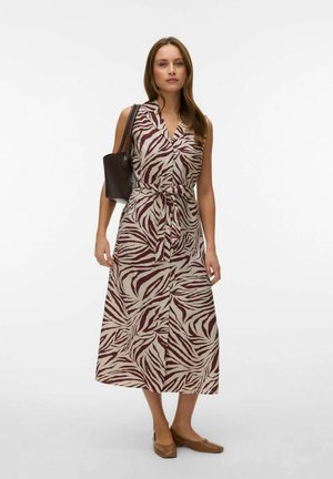 Donna che indossa un abito midi senza maniche con stampa zebrata marrone e beige, cinturetta annodata, borsa a tracolla marrone e ballerine marroni, in piedi su sfondo bianco.