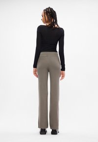 Crna majica dugih rukava i maslinasto zelene hlače s visokim strukom od rebrastog materijala. Hlače imaju široki kroj i glatku teksturu. Crna obuća.